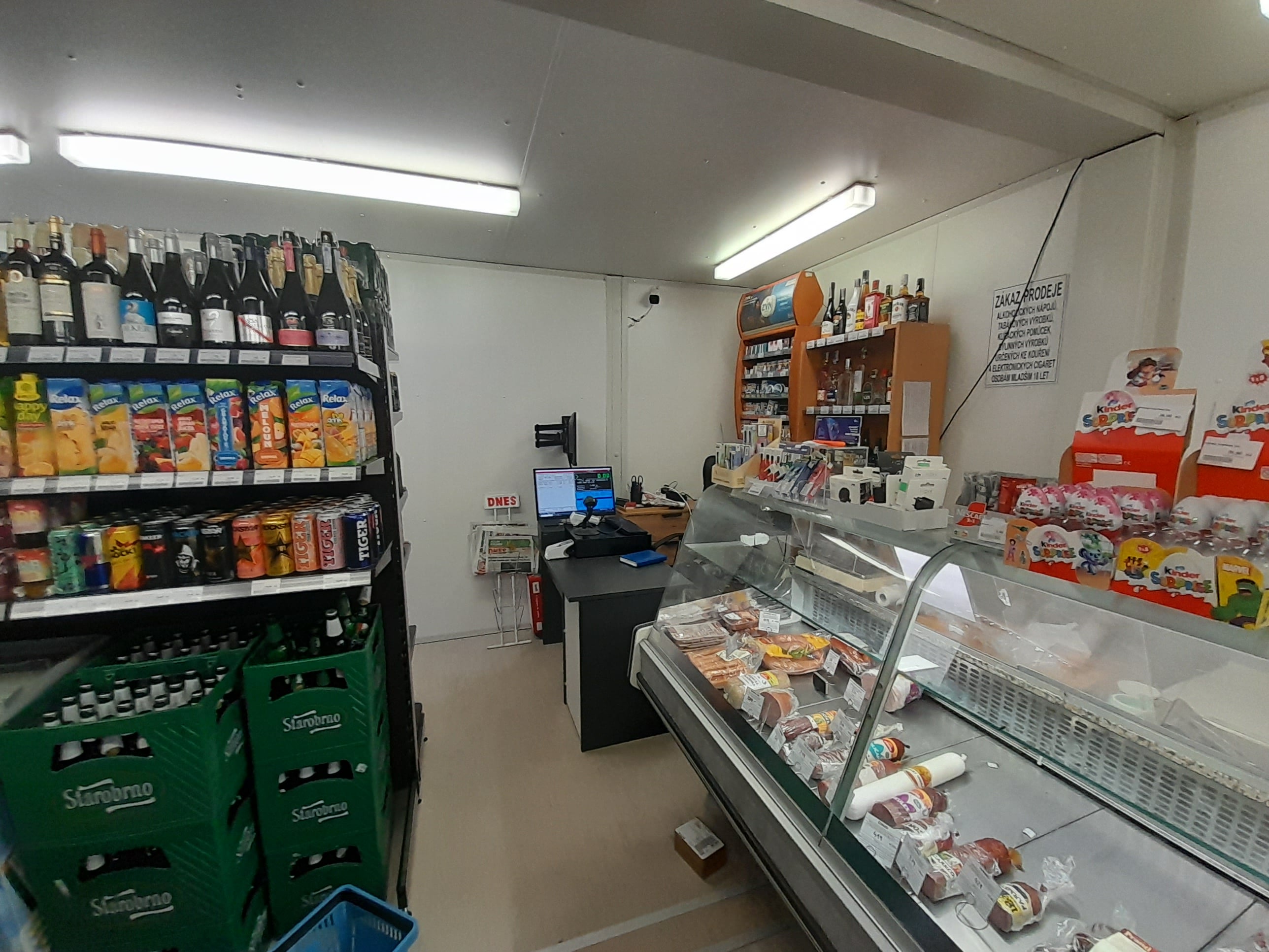 Interiér modulární prodejny – regály a chladicí pult s obsluhou Interiér dočasné prodejny v modulárním kontejneru – regály se zbožím, chladicí pult s lahůdkami a pokladní zóna