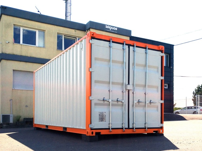 Designový skladový kontejner bílé barvy s oranžovým ohraničením, stojící před budovou.